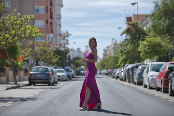 Young and beautiful woman in a purple dress and heels, posing in the middle of a city road. Concept...