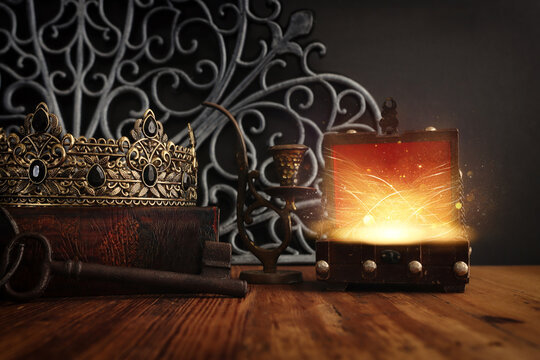 low key image of beautiful queen or king crown over antique book next to wooden treasure chest. vintage filtered. fantasy medieval period