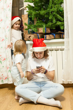 A teenage girl in a red cap plays the phone, two little girls play together. Christmas eve
