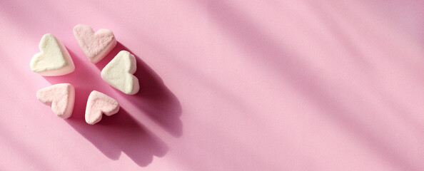 Delicate pink and white marshmallows in the shape of a heart on a pink background with copy space, closeup. Valentine's Day symbols tender marshmallow sweets heart shape on banner.