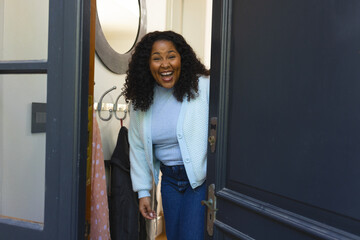 Happy african american woman opening door and laughing in sunny house
