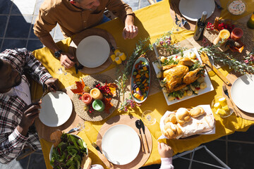 Happy diverse male and female friends serving thanksgiving celebration meal in sunny garden