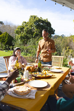 Happy diverse male and female friends toasting during thanksgiving celebration meal in sunny garden