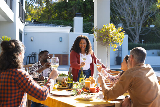 Happy diverse male and female friends toasting during thanksgiving celebration meal in sunny garden