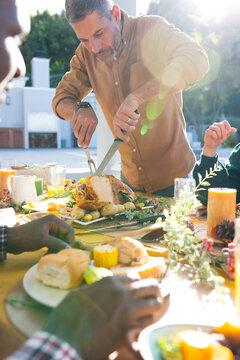 Happy caucasian man cutting meat during thanksgiving celebration meal in sunny garden