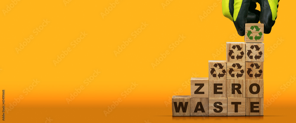 Poster gloved hand arranging wood blocks with text zero waste and recycling symbols on an orange and yellow