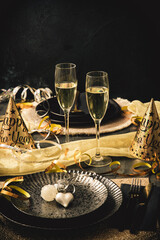 Table setting with decorative heart, two glasses with sparkling wine and party decoration, black and gold colors, vertical with copy space