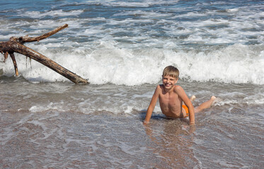 A teenager boy lies in the sea in the waves and looks at the camera, rest with children, selective ficus