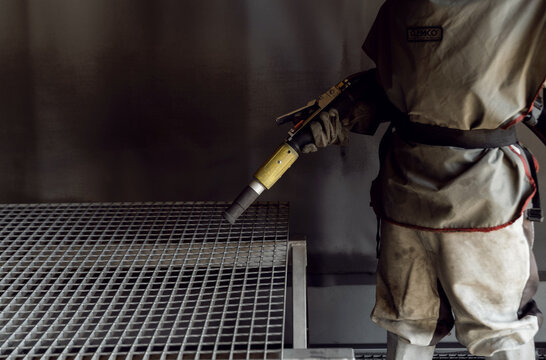 sandblasting a metal surface in a workshop close-up. a master in special clothing holds a sandblasting hose in his hands. working with sandblasting - Powered by Adobe