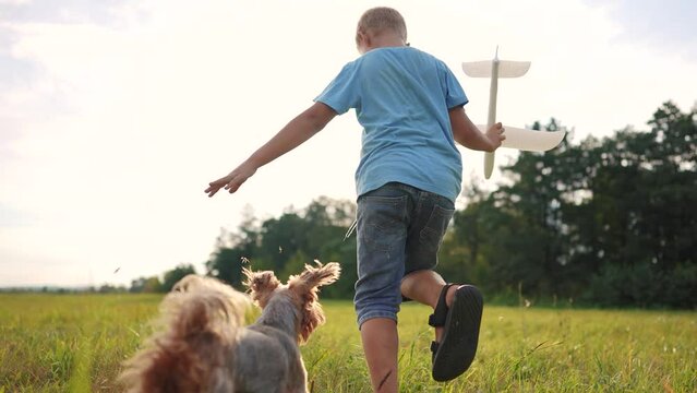 the boy runs with the plane and the dog. happy family kid dream concept. boy son running across a field of green grass in the park playing with a toy airplane and a pet dog lifestyle
