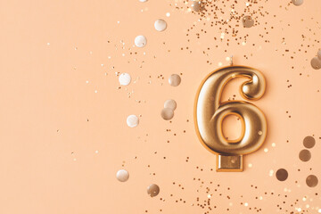 Gold candle in the form of number six on peach background with confetti.