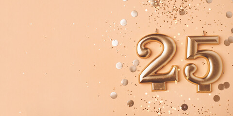 Gold candles in the form of number twenty five on peach background with confetti. 25 years anniversary celebration.