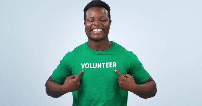 Volunteer, black man smile and laughing face with pointing to NGO, logo and charity tshirt in studio. Nonprofit, portrait and African male person happy from activist platform with blue background