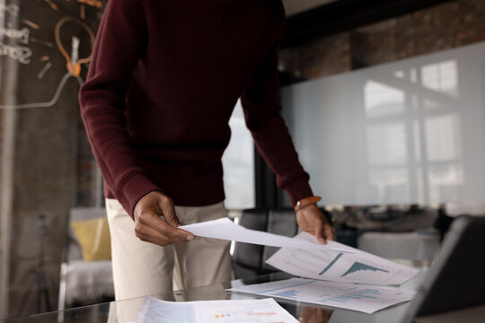 Midsection of african american casual businessman looking at documents at home office, copy space