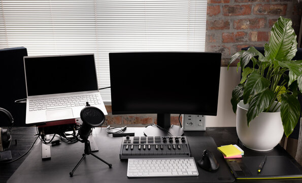 Podcasting set up with computers, keyboard and microphone on desk with plant at home