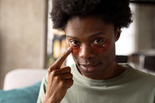 Portrait of african american man sitting on couch at home applying under eye masks