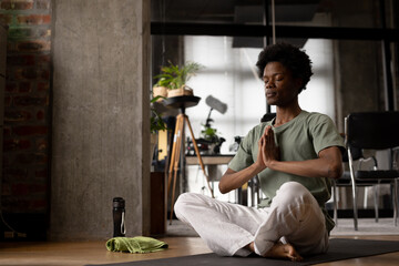 Happy relaxed african american man practicing yoga meditation sitting on floor at home, copy space