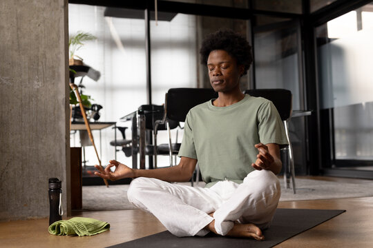 Happy relaxed african american man practicing yoga meditation sitting on floor at home