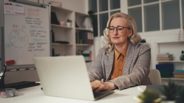 Exhausted businesswoman in her 50s typing on laptop, feeling tired of work