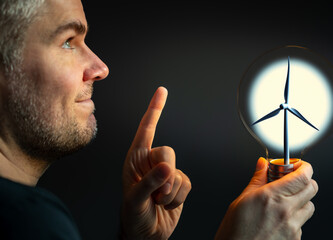 Man holding a light bulb with a wind turbine inside. Symbol for producing clean energy.