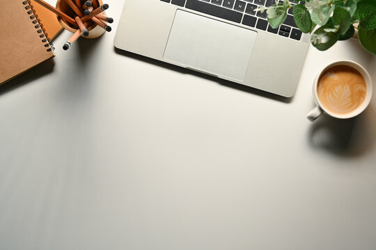 Simple workspace with laptop, notepad, coffee cup and potted plant on white table. Top view with copy space for text