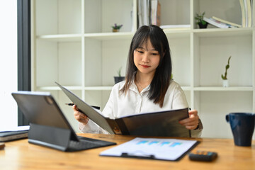 Obraz na płótnie Canvas Concentrated asian female employee reviewing financial reports at her workplace