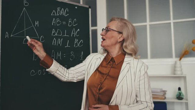 Geometry teacher in her 50s explaining material near chalkboard during lesson