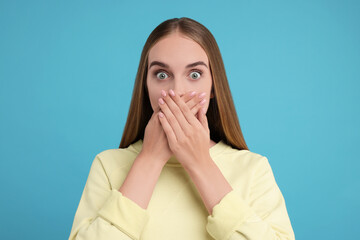 Embarrassed woman covering mouth with hands on light blue background