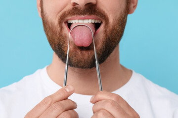 Man brushing his tongue with cleaner on light blue background, closeup - obrazy, fototapety, plakaty