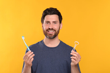 Happy man with tongue cleaner and plastic toothbrush on yellow background