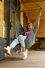 happy girl relaxing in a hammock on the terrace of her wooden country house on sunny summer day