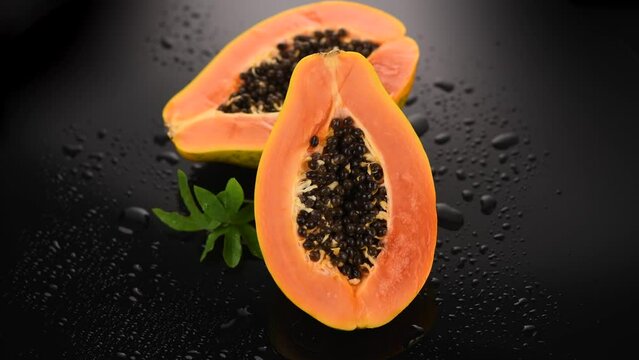 Papaya fruit on wet black background with water drops. Halved fresh organic Papaya exotic fruits close up. Slow motion, rotating. 