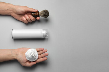 Man with shaving foam, brush and bottle on light grey background, top view. Space for text