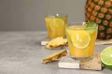 Glasses of tasty pineapple cocktail with mint and lime on light grey table. Space for text