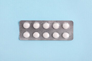 White pills in blister on light blue background, top view