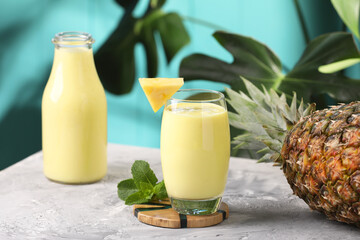 Tasty pineapple smoothie, mint and fruit on grey textured table