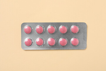 Pink pills in blister on beige background, top view