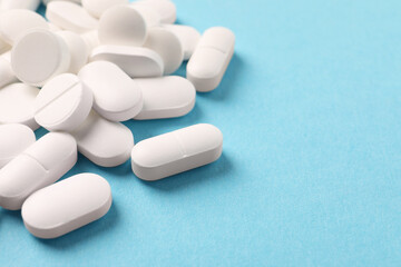 Pile of white pills on light blue background, closeup. Space for text