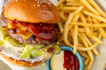 Beef burger with lettuce and pickles with fries and sauce on a gray-blue background