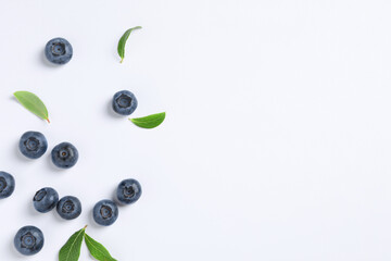 Tasty fresh blueberries with green leaves on white background, flat lay. Space for text