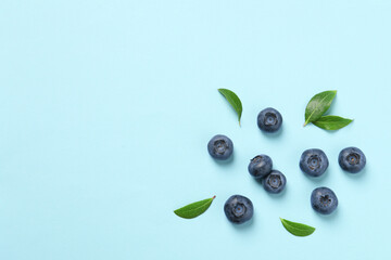 Tasty fresh blueberries with green leaves on light blue background, flat lay. Space for text
