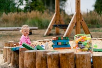 A cute little girl smiling and enthusiastically playing in wooden sandpit in nature overlooking a...