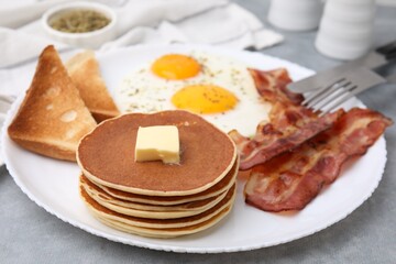 Tasty pancakes served with fried eggs and bacon on grey table, closeup