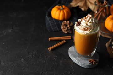 Glass of pumpkin spice latte with whipped cream and ingredients on black table. Space for text