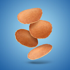 Tasty fresh pancakes falling on blue background