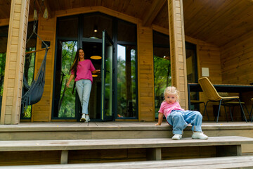 smiling cute little girl in stylish clothes on the terrace of a wooden house in the woods 