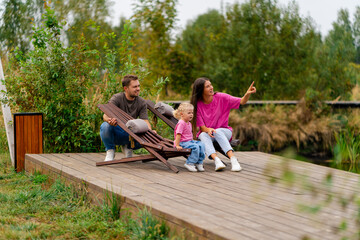 young family man and woman playing together with their daughter relaxing on the shore of lake in...