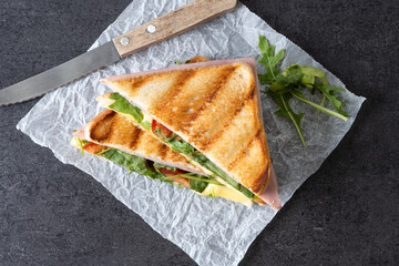 Panini sandwich with ham, cheese, tomato and arugula on black slate background. Top view