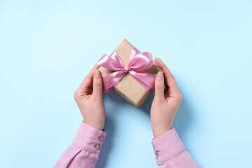 Woman holding gift box with pink bow on light blue background, top view