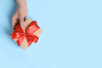 Woman holding gift box with red bow on light blue background, top view. Space for text